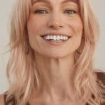Blonde woman with wavy hair wearing lace top, smiling.